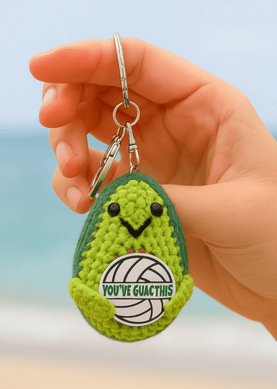 Hand holding a green avocado-shaped keychain with text against a blurred background